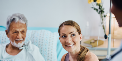 Happy woman and her ill father holding hands while communicating with a doctor in hospital ward.