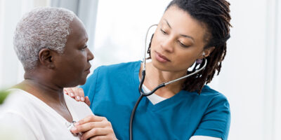 A caring mid adult female home healthcare nurse uses a stethoscope to check the heart and lungs on a senior female patient