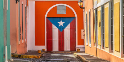 Charming cobblestone street in Old San Juan, Puerto Rico, with colorful colonial buildings featuring door painted with the Puerto Rican flag, vibrant scene full of culture and history