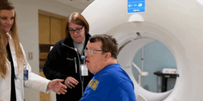Patient with Down syndrome being guided into MRI by two health care professionals